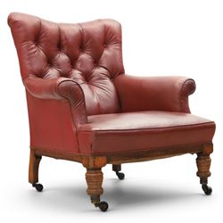 Early 20th century style oxblood red leather Chesterfield armchair, deep buttoned shaped back over padded scroll arms and loose seat cushion, raised on turned mahogany front supports with brass caps and castors