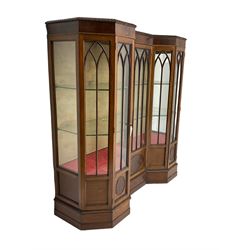 Early 20th century mahogany Gothic style display cabinet, faceted reverse break front, enclosed by three doors with pointed arch astragal glazing, on stepped and moulded plinth base