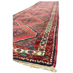 Persian red ground runner, the field decorated with eight interconnected stylised floral lozenge medallions, within three border bands decorated with Boteh and stylised flowerhead motifs 