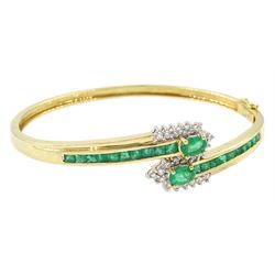 14ct gold emerald and diamond crossover bangle, two oval cut emeralds with round brilliant cut diamond surround, with channel set calibre cut emerald shoulders, stamped 585