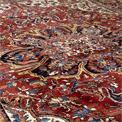 North West Persian Ahar hand-knotted carpet, madder red ground, with a large central shaped floral medallion with pendants, surrounded by angular scrolling foliate motifs incorporating rosettes, palmettes and stylised flowerheads, enclosed by ivory spandrels and a dark navy border with repeating geometric floral motifs and meandering vines, flanked by narrow patterned guard stripes, with cotton fringes