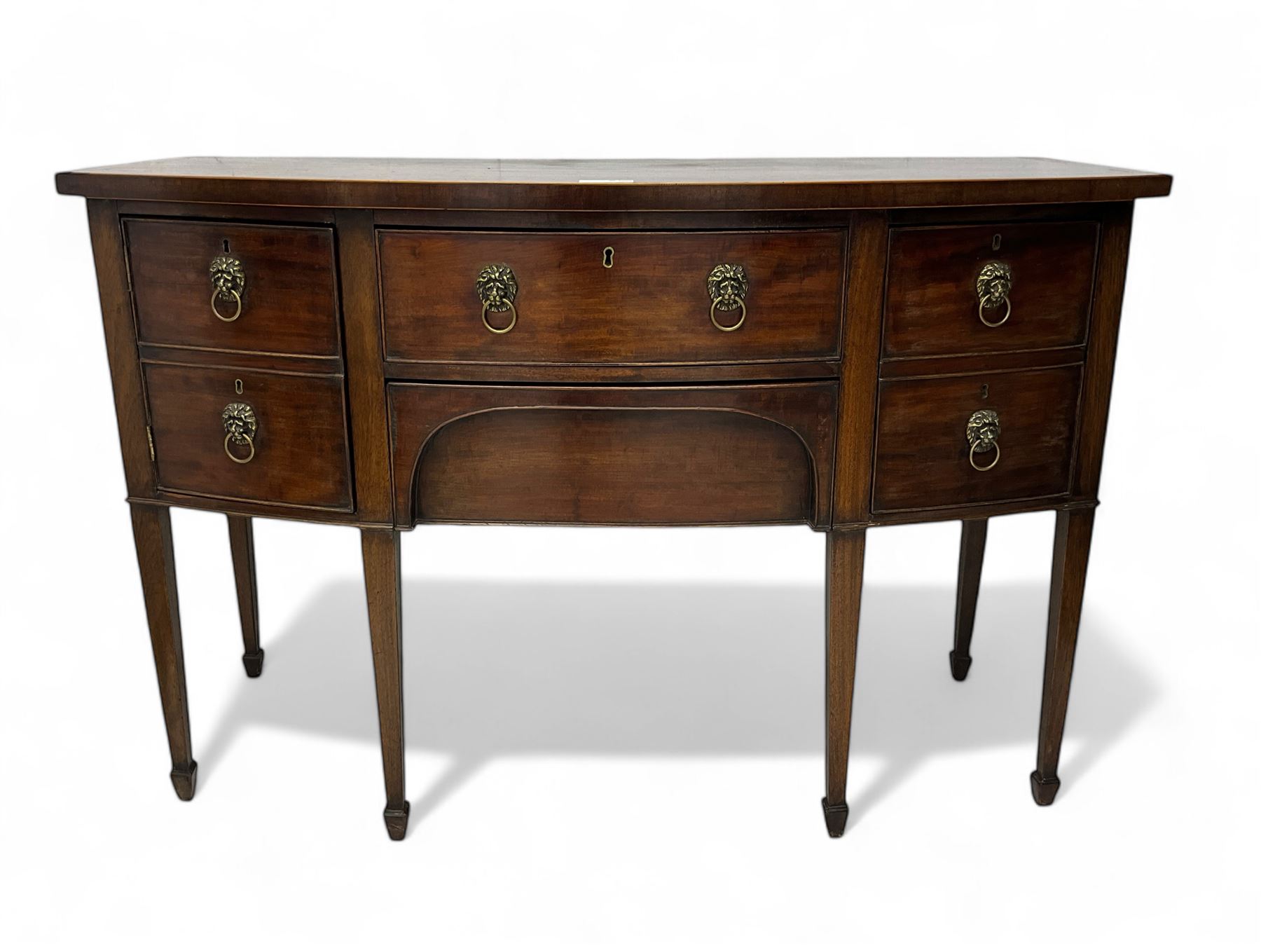George III mahogany bow-fronted sideboard, mahogany banded top over three drawers and cupboard, fitted with lion mask and hoop handles, on square tapering supports with spade feet