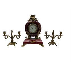 A 20th century three-piece clock garniture, with an 8-day timepiece movement and cylinder platform escapement in a circular porcelain case on a shaped rectangular plinth raised on four scroll feet, with gold painted decoration in the form of leaves and flowers,  with a four inch white dial, Roman numerals and quarter Arabic’s, minute track and spade hands, bevelled glass and brass bezel, movement wound and set from the rear, with a pair of corresponding two light candelabra. No Key.