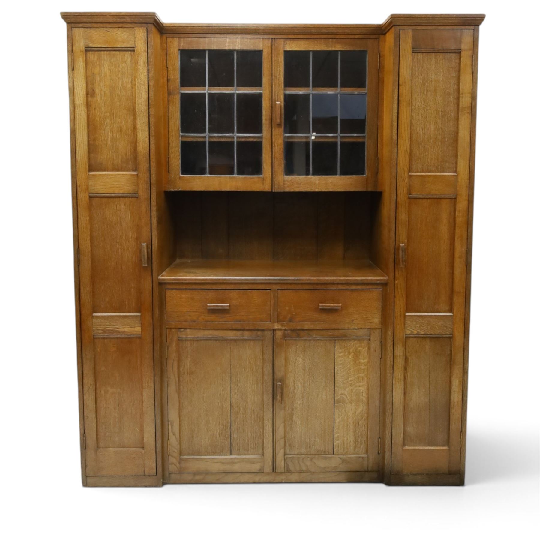 Arts & Crafts oak housekeeper’s cupboard, stepped moulded cornice over twin leaded glazed doors enclosing shelved interior, flanked by narrow panelled cupboards, open recess below over two drawers and twin panelled cupboard doors, with rectangular handles