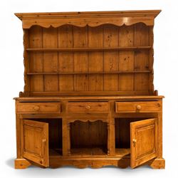 Late 20th century pine dresser, the plate rack with two fixed shelves and shaped apron over panelled back, base fitted with three drawers over two cupboard doors and central open niche flanked by turned uprights, on plinth base with shaped apron