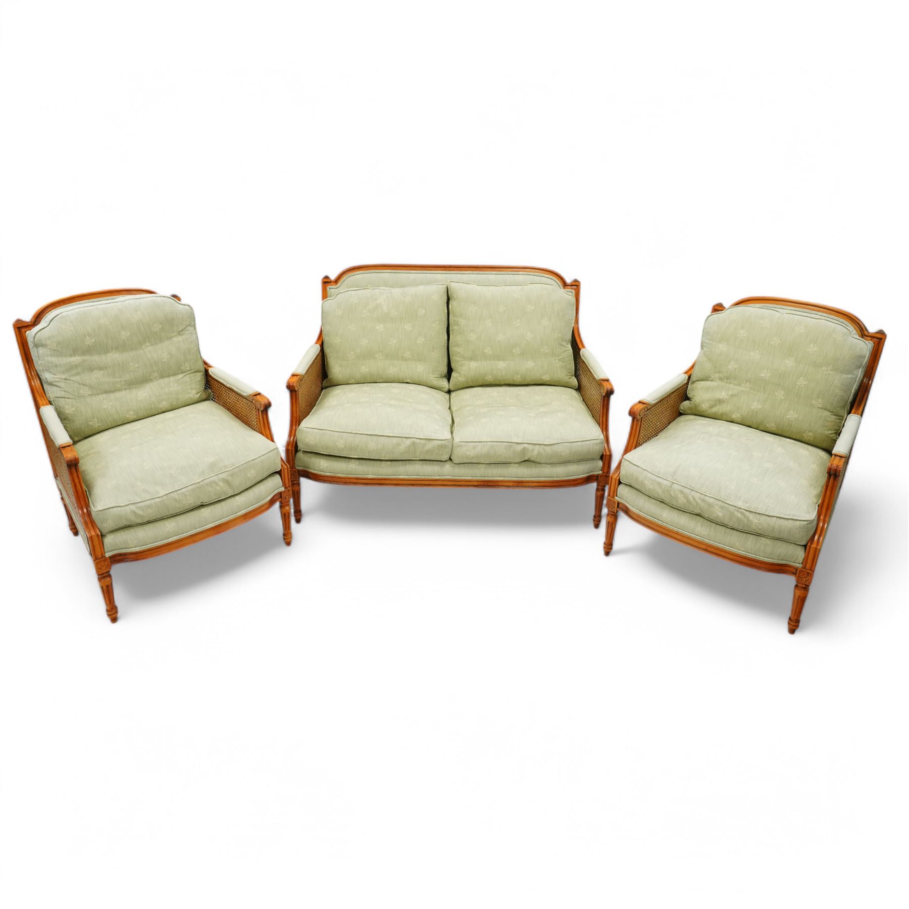 French Empire design varnished wood three piece lounge suite comprising of two cane armchairs and matching sofa, carved top rails with foliate terminals, cane side panels and padded scroll arms, upholstered in a green brocade with matching piping, on fluted legs