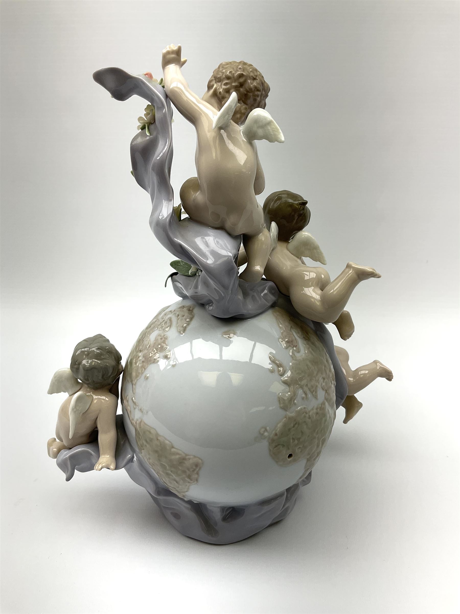 A Lladro mantel clock modelled as a globe with inset clock, surmounted by four putti and floral garlands, with blue printed mark and impressed 5973 beneath, H29cm.
