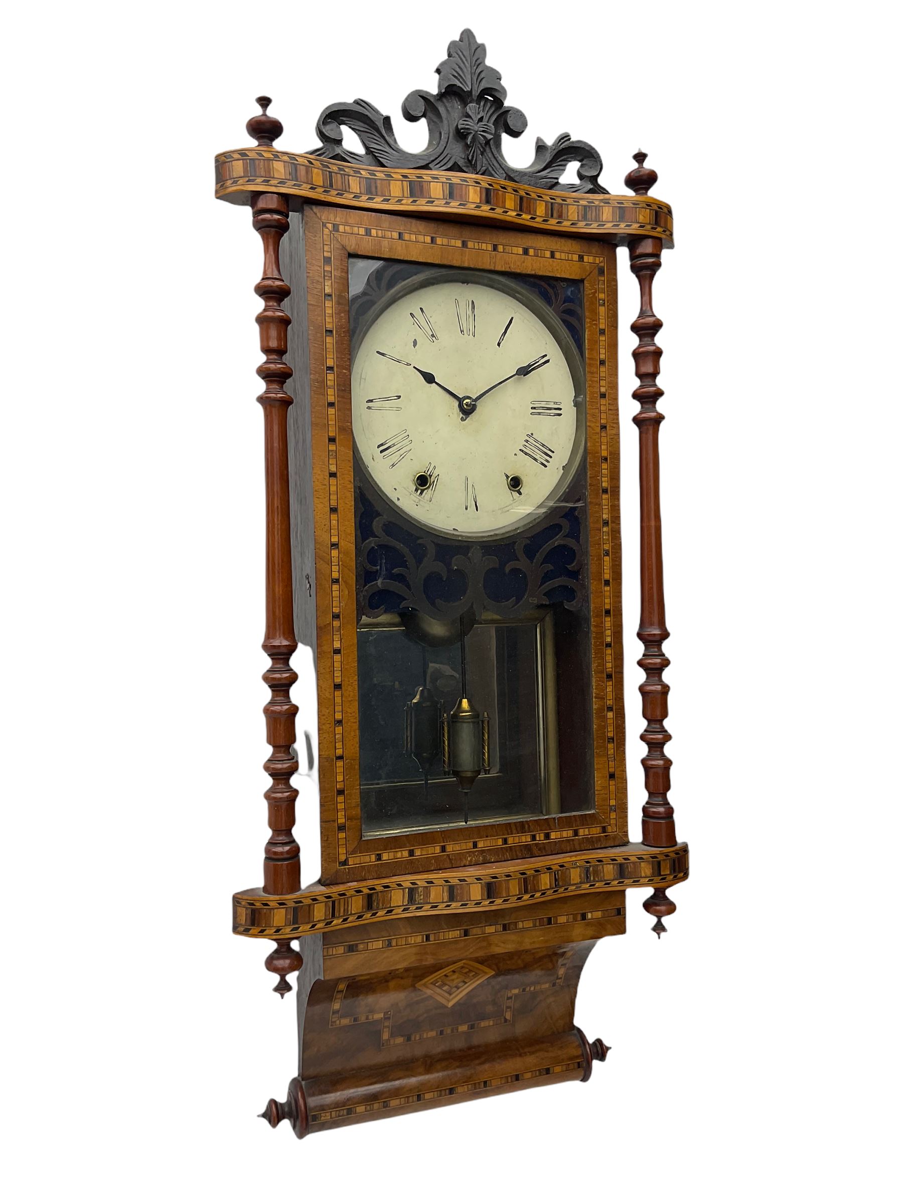 A late 19th century spring driven American Eight-day wall clock, striking the hours on a bell, in a parquetry case with contrasting oak, maple, walnut, and other hardwoods, with a flat top, carved cresting and finials rectangular glazed door flanked by finely turned pilasters, with a painted dial with roman numerals and minute track, steel spade hands and faux mercury pendulum reflected in a rear case mirror.   


