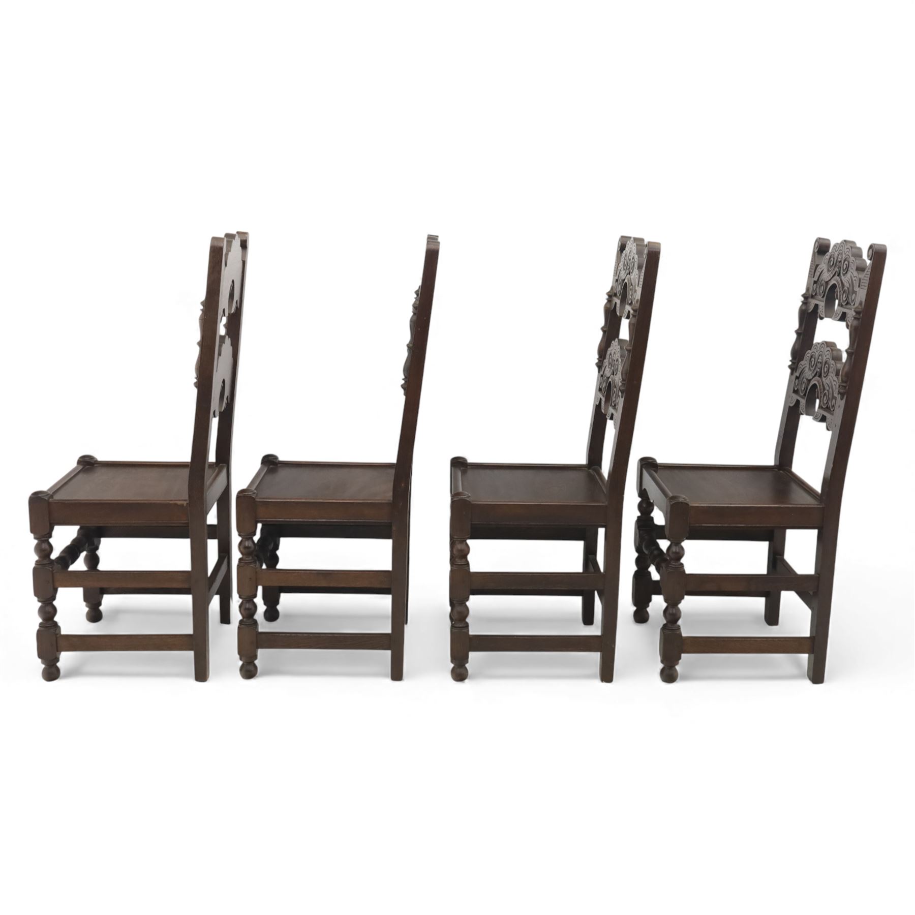 Early 20th century set of seven Jacobean Revival oak chairs, comprising pair of cavers and five chairs, each with carved mask and scroll decoration to the crest and and back rail, plain oak seat, upon turned front legs and block rear legs with conforming stretchers