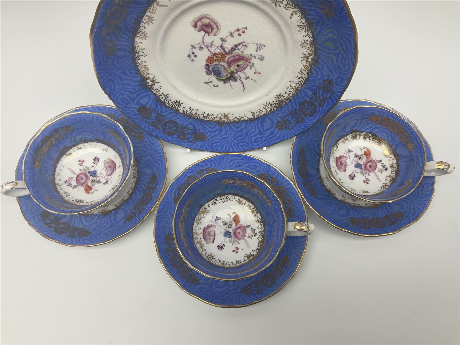 Set of three Victorian teacups and saucers, with matching dessert plate, decorated with a watered silk blue boarder and hand painted floral sprays to the centre 