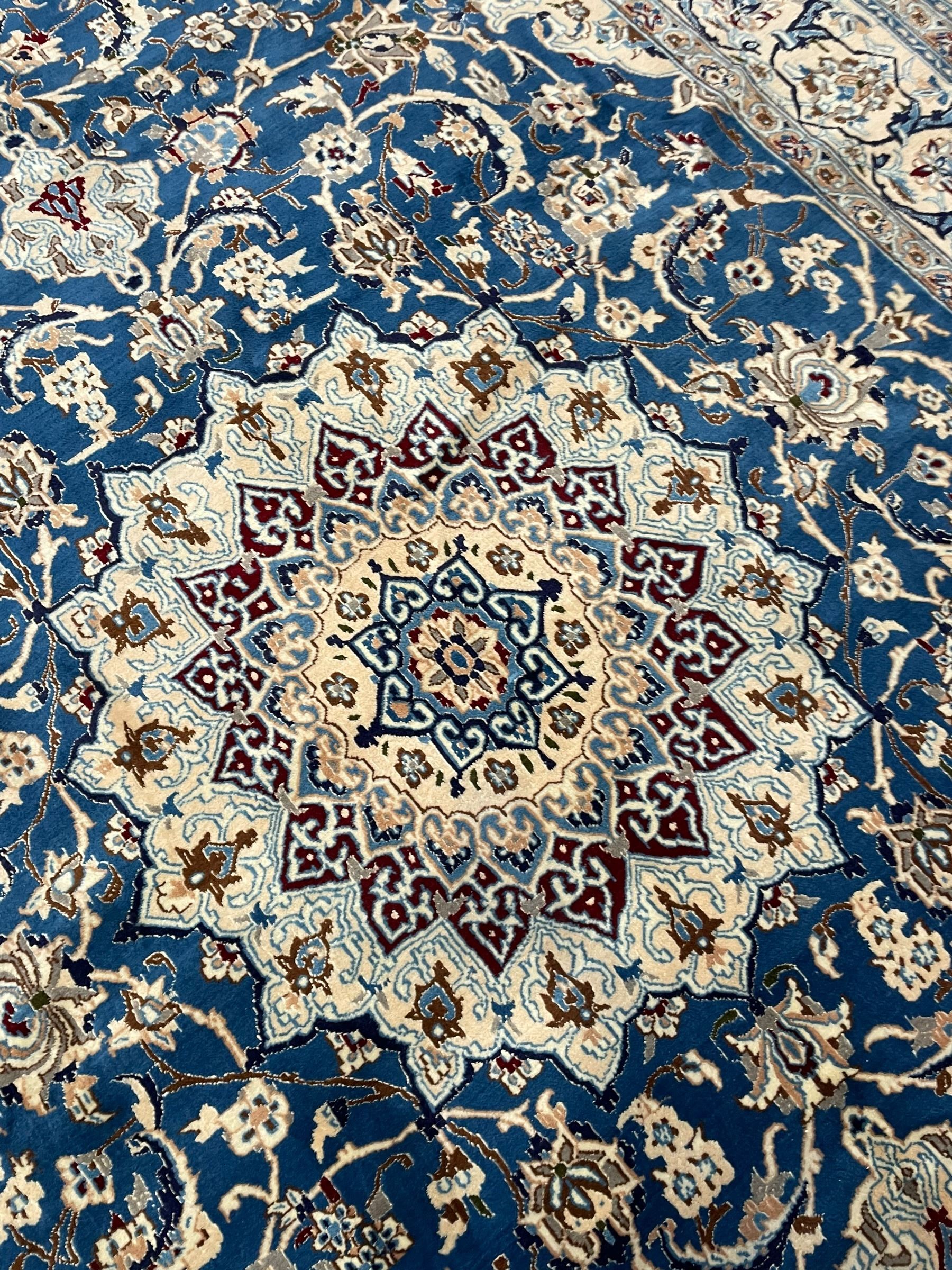 Persian Kashan blue ground rug, central floral rosette medallion within a field of swirling branches and palmettes, the border with trailing pattern interspersed with stylised plant motifs
