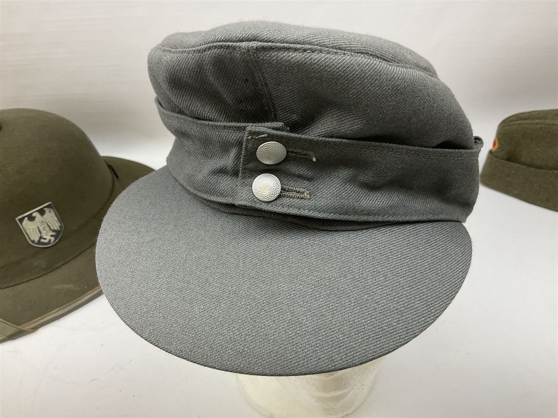Five reproduction German WW2 hats comprising Wehrmacht olive tropical helmet, Heer officer's peaked cap, two M43 caps and Field side cap (5)