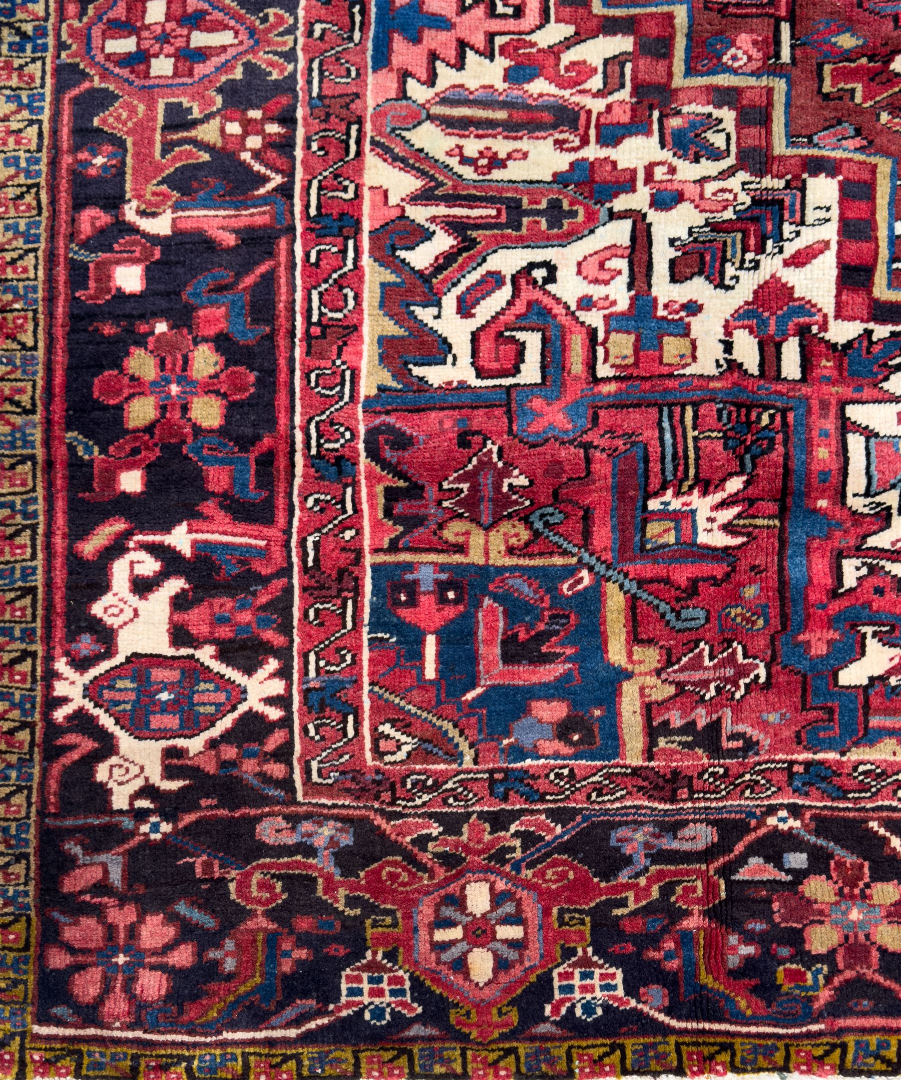 Northwestern Persian Heriz hand-knotted carpet, red madder field with a bold stepped medallion in indigo, ivory, and terracotta, flanked by angular floral motifs and stylized leaves, the spandrels set within a dark indigo border of rosettes and angular vine motifs between narrow guard stripes, 340cm x 245cm 