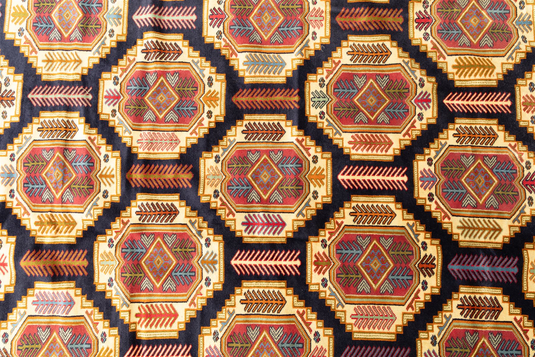 Central Asian Turkmen, main field with octagonal guls enclosing hooked diamond motifs in shades of madder gold, ivory, and indigo set against a dark ground within multiple polychrome borders of geometric devices and stepped motifs 