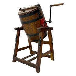 19th century oak and cast iron rotary butter churn, with coopered barrel body, domed lid with filler opening and cast iron securing arms, on tilting iron-mounted frame with crank handle and support rails