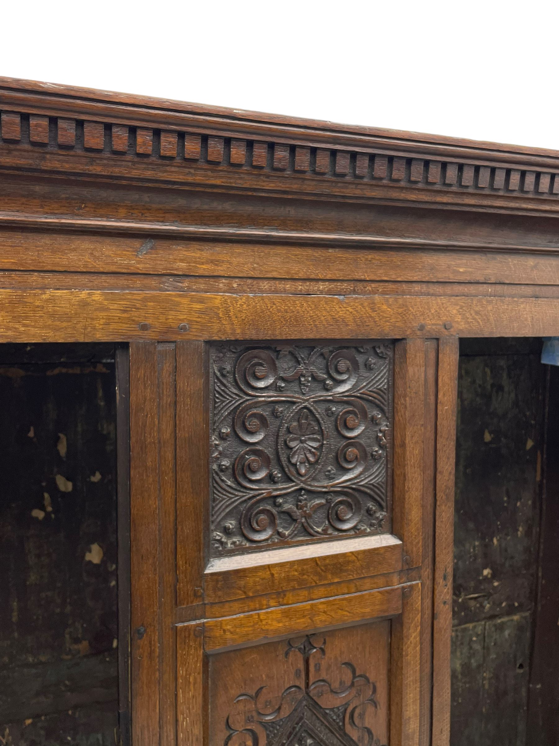 Large 18th century and later oak livery cupboard, projecting moulded and dentil cornice, sunken fillet moulded frame, triple vertical panelled central upright, enclosed by two doors each with five panels, the top row of panels carved with stylised scrolls, the lower panels carved with foliate lozenges, on shaped bracketed skirt base 