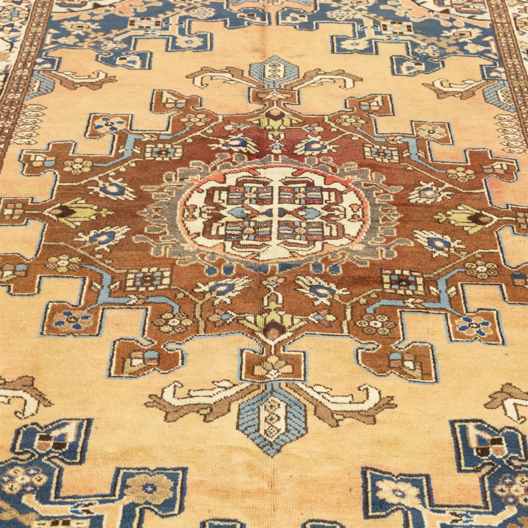 North West Persian Tafresh hand-knotted rug, pale apricot field with central stepped medallion enclosing stylized floral and angular motifs framed by indigo spandrels and multiple stylized floral borders, cotton fringe ends 