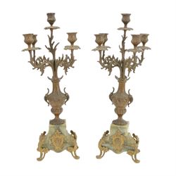 French-Edwardian green onyx clock garniture with a shaped case surmounted by a cast patinated figure of  a maiden in 18th century dress, with gilded scroll feet and conforming mounts, porcelain dial with Arabic numerals and floral decoration, twin train rack striking movement sounding the hours and half-hours on a bell, with a matching pair of five light candelabra. With pendulum.    