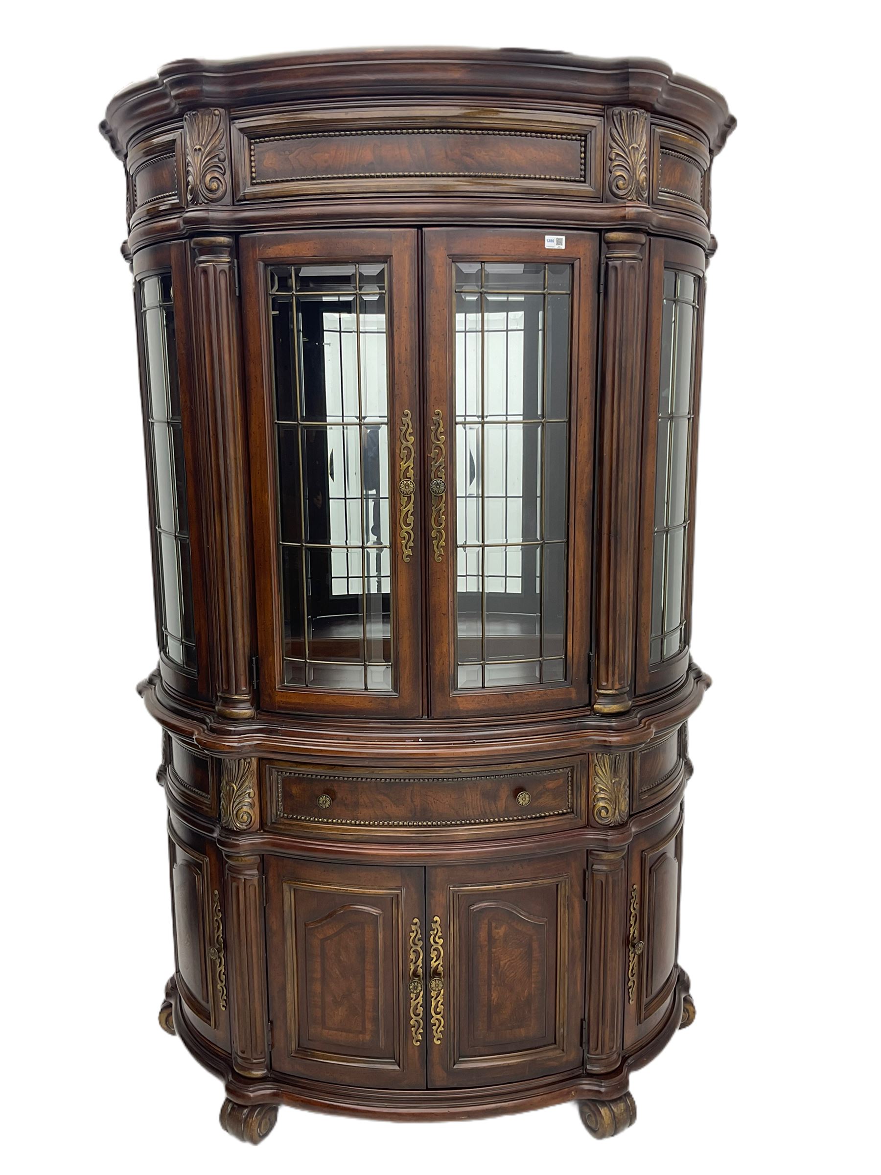  Kevin Charles American walnut demi lune display cabinet with illuminated interior, projecting cornice, two bevel edge glazed doors enclosing two adjustable shelves above single drawer and four cupboard doors with wine rack, carved scrolling supports