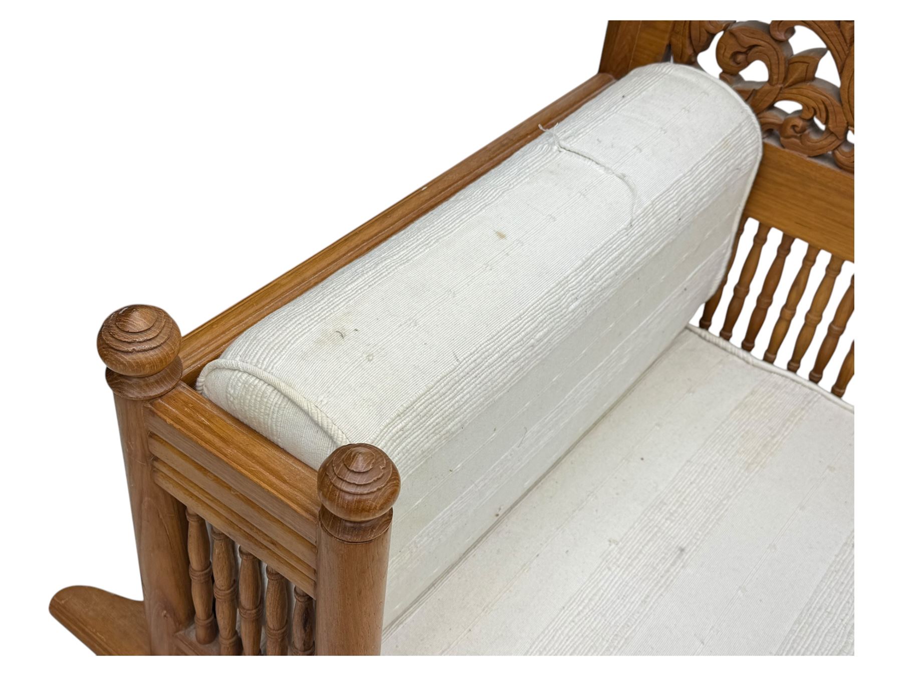 Early 20th century carved teak Howdah elephant chair, with pierced floral and foliate carved backrest, spindle gallery arm supports, cream upholstered cushions, splayed legs on a curved reeded base 