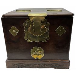 Chinese brass bound hardwood travelling vanity box of oblong form with side carrying handles, the hinged top opening to reveal a hinged toilet mirror above a pair of doors enclosing various drawers and compartments on a stepped base with carved and moulded decoration W28cm H23cm D38cm