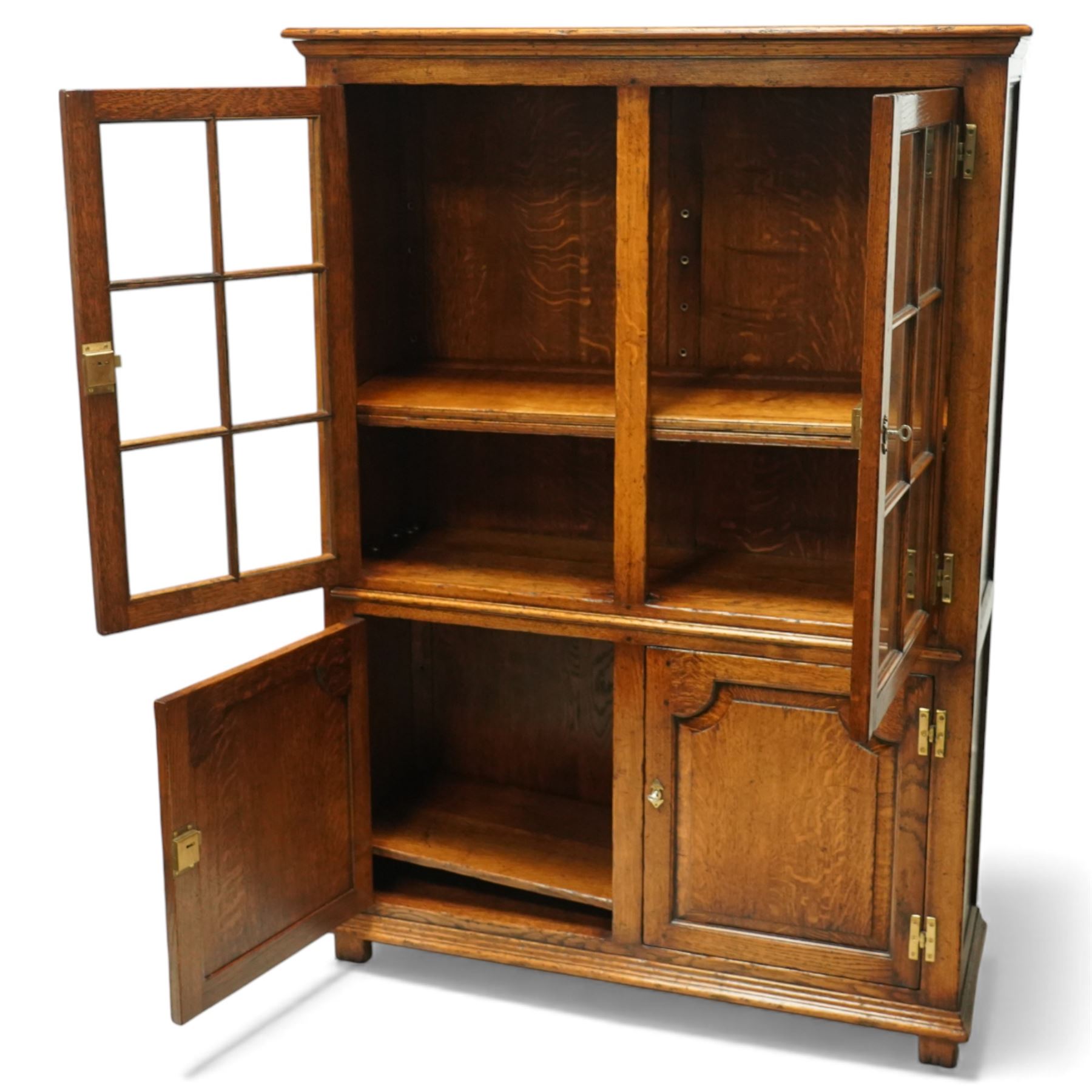 Late 20th century oak cabinet in the manner of Titchmarsh & Goodwin, rectangular top over a pair of nine-pane glazed doors enclosing adjustable shelves, above two moulded panel cupboard doors, raised on block feet