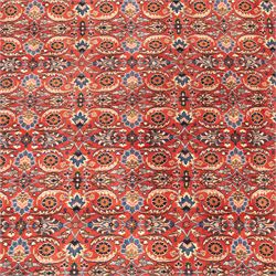North West Persian carpet, the red field decorated with an all over repeating design of palmettes, rosettes and curling serrated leaves in indigo, ivory and ochre tones, enclosed by an indigo scrolling floral border and ivory flowerhead guard bands