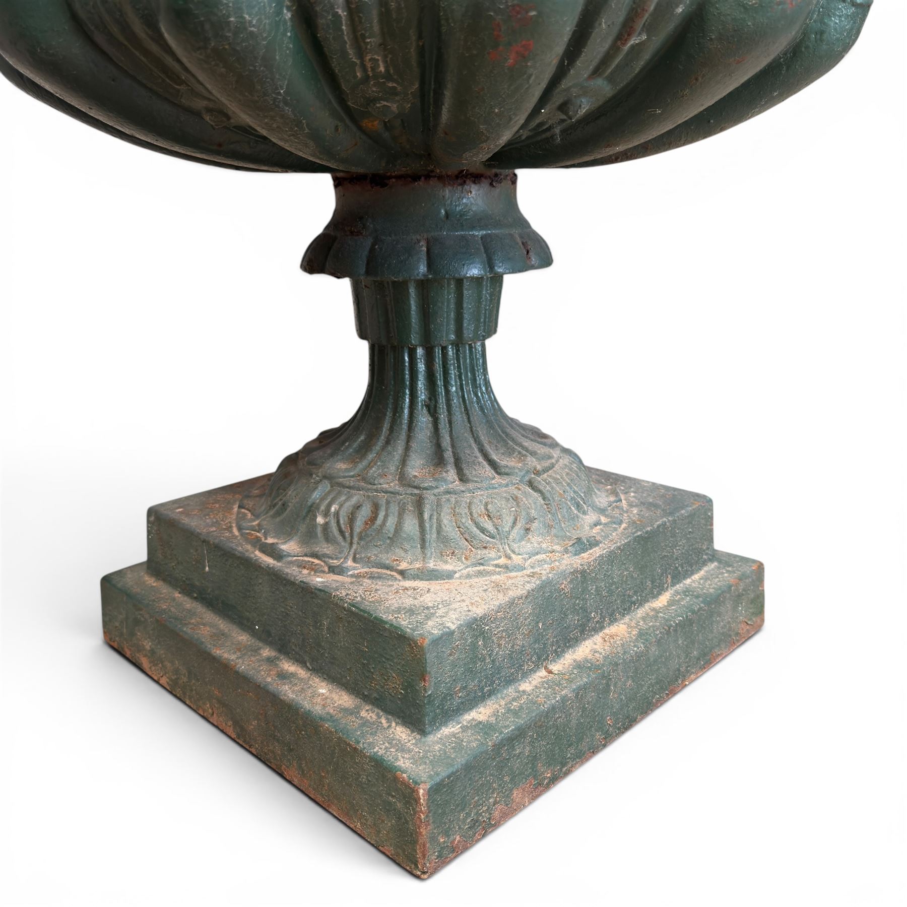 Pair of Victorian cast iron campana garden urns, the flared rim with repeating stylised anthemion motifs with scrollwork, over a deep gadrooned and Aesthetic moulded underbelly, fluted and foliate lower bowls on square pedestal bases, in antique green-painted finish