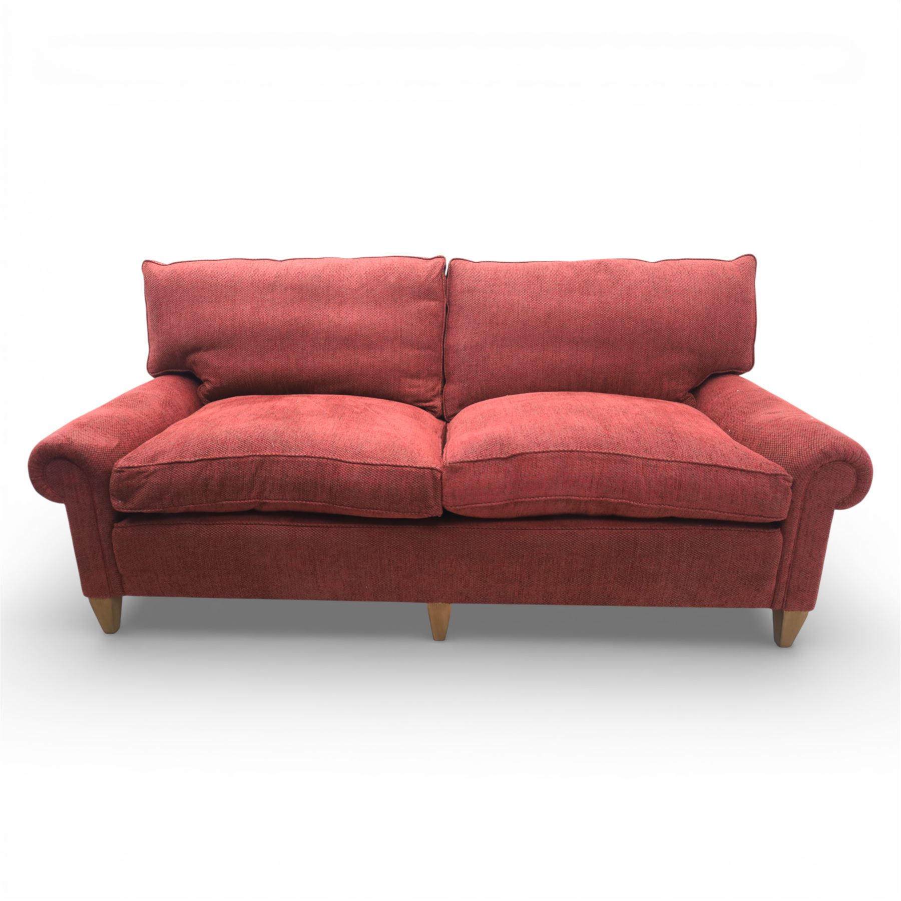 Late 20th century three seat sofa upholstered in red fabric, with gently rounded scroll arms, loose seat and back cushions, raised on tapered wooden legs