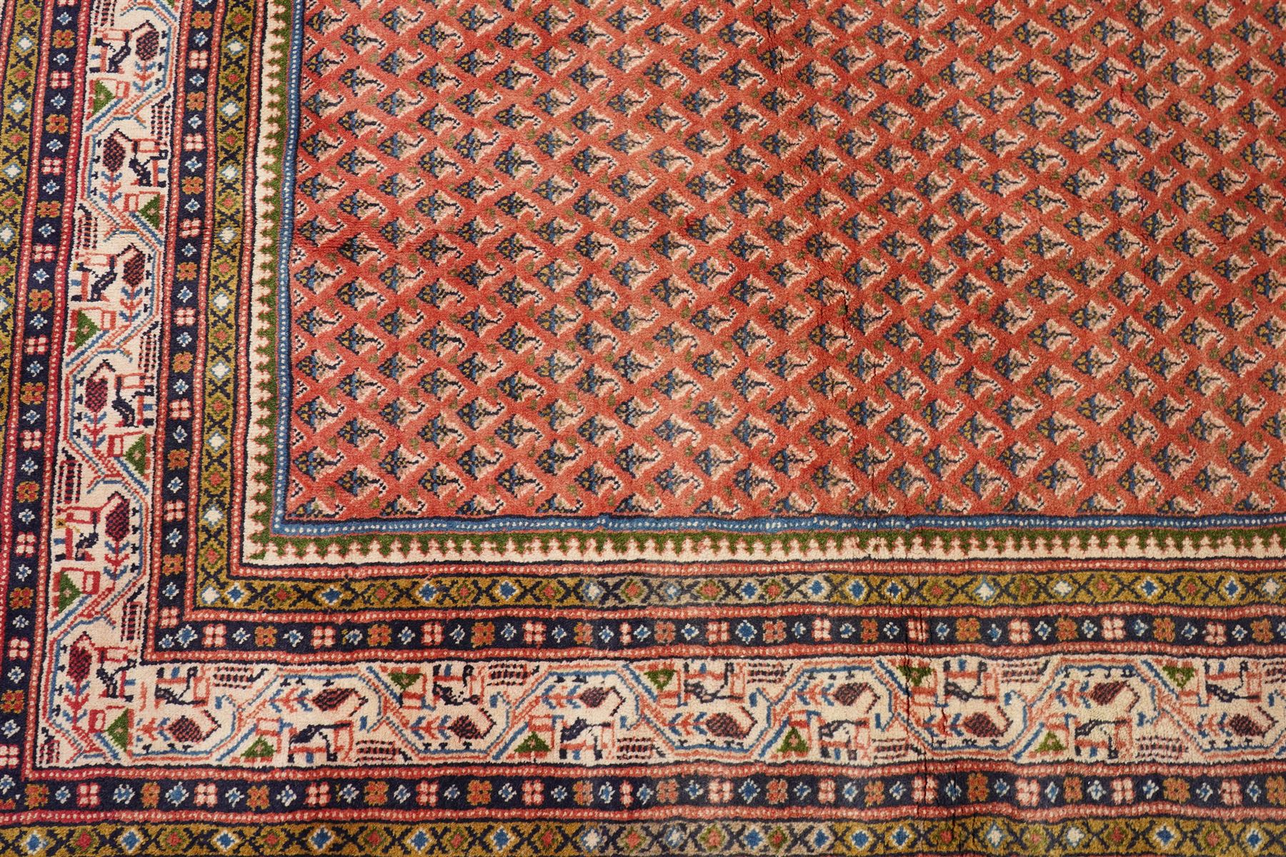 West Persian Boteh-Mir hand-knotted rug, madder red field densely decorated with a repeating lattice of of small boteh motifs arranged in diagonal rows enclosed by a broad border of stylized geometric devices and angular floral ornament between multiple guard stripes with cotton fringe ends