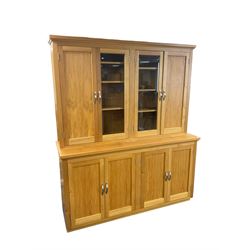 Light oak wall display cabinet, the top section fitted with two double cupboards enclosed by glazed and panelled doors, the lower section with two panelled double cupboards
