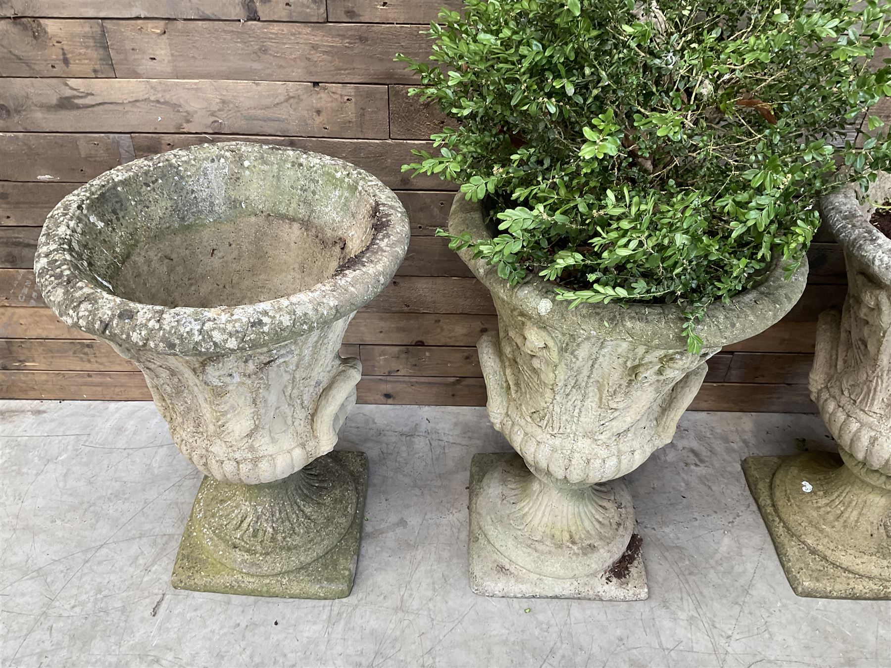 Set of four Victorian design cast stone Grecian urns, tapering form cast with figures and handles, square plinth bases