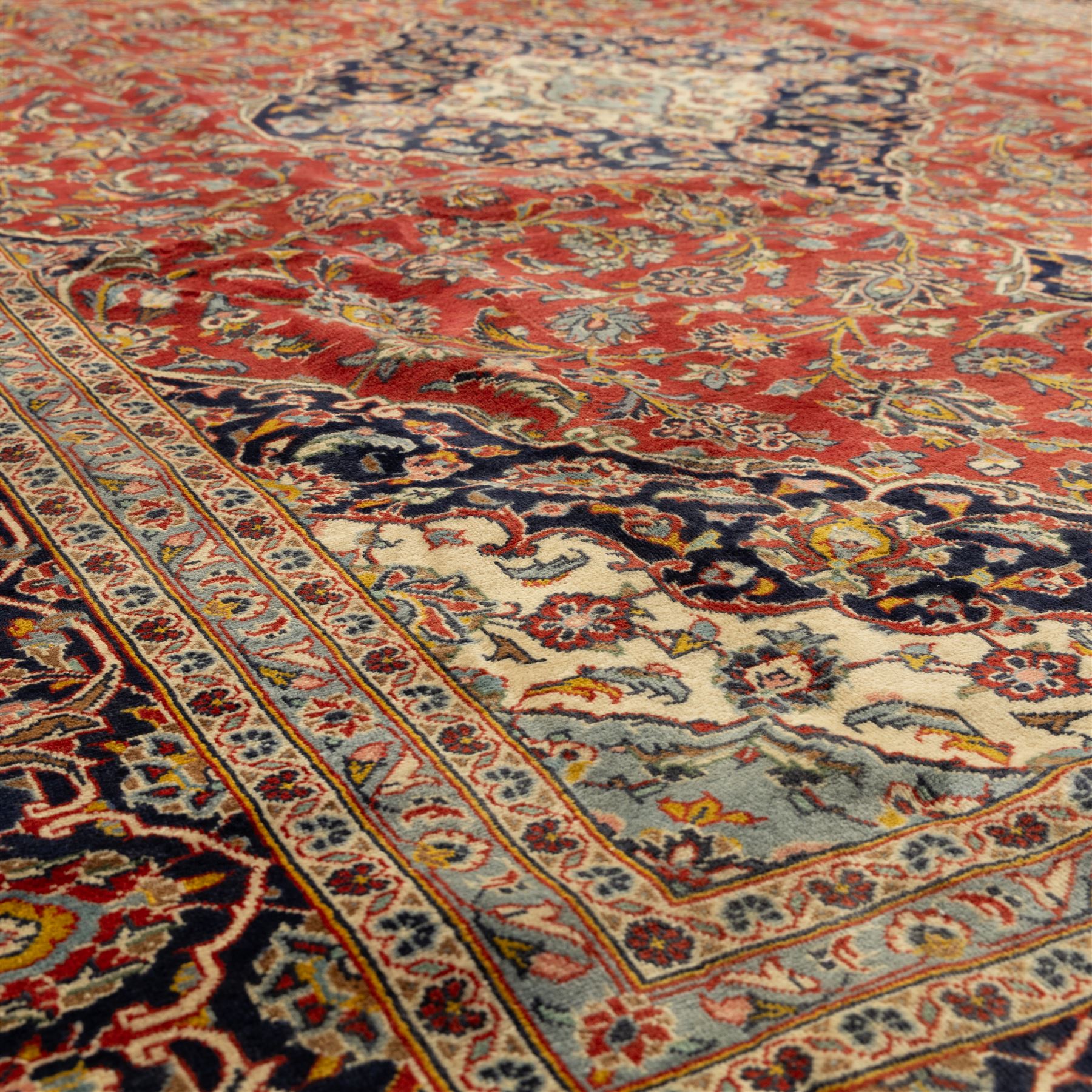 Persian Kashan carpet, the field in rich rust tone centred by an ivory and blue medallion with palmette extensions, surrounded by intricate foliate arabesques and stylised blooms, within triple floral borders incorporating palmettes and interlaced tendrils, woven in the region of Kashan