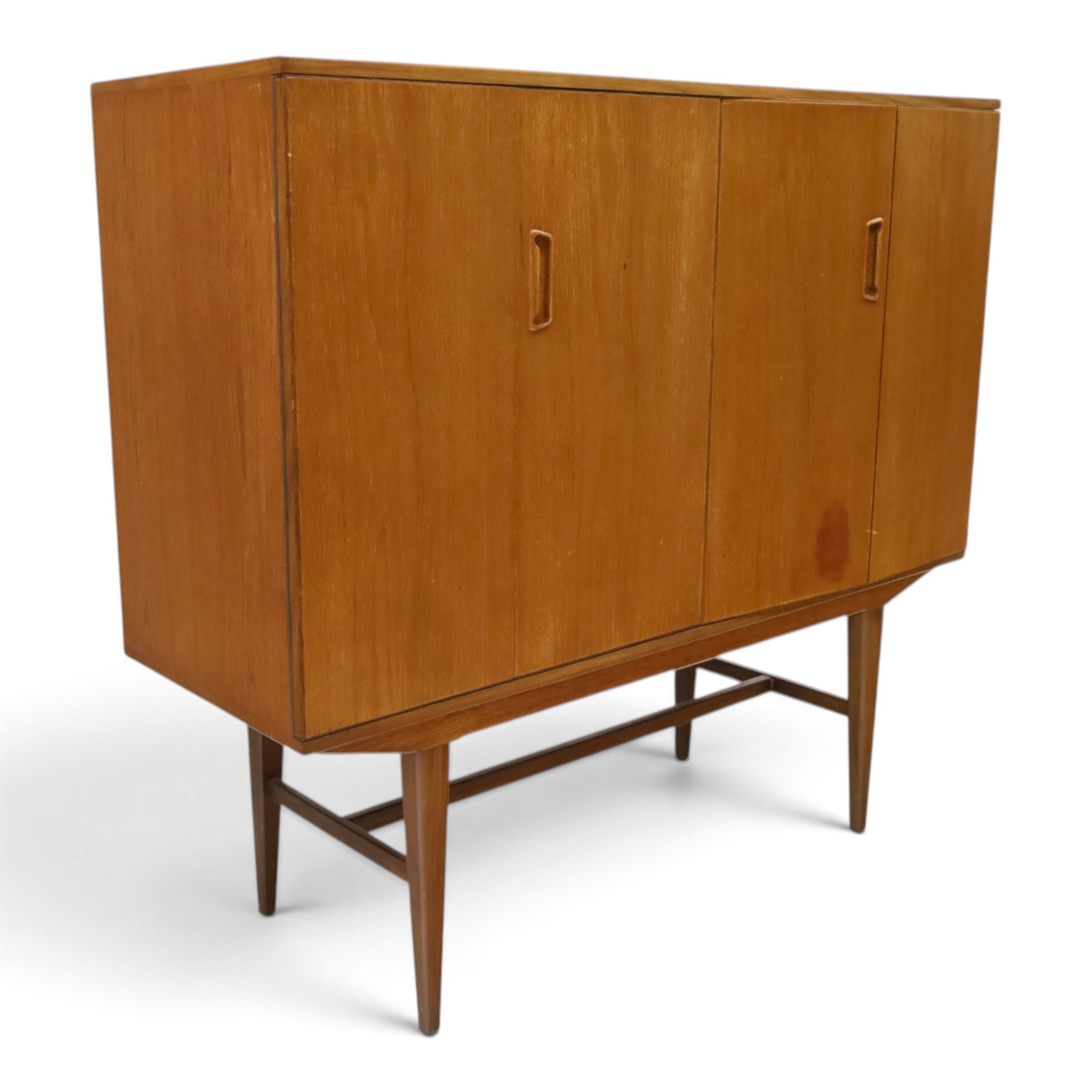 Alfred Cox - mid-20th century teak cabinet, rectangular top over two bifold doors with inset handles, opening to reveal three central graduating drawers surrounded by assorted shelves, raised on tapering supports united by H-stretcher, stamped to inside of drawer