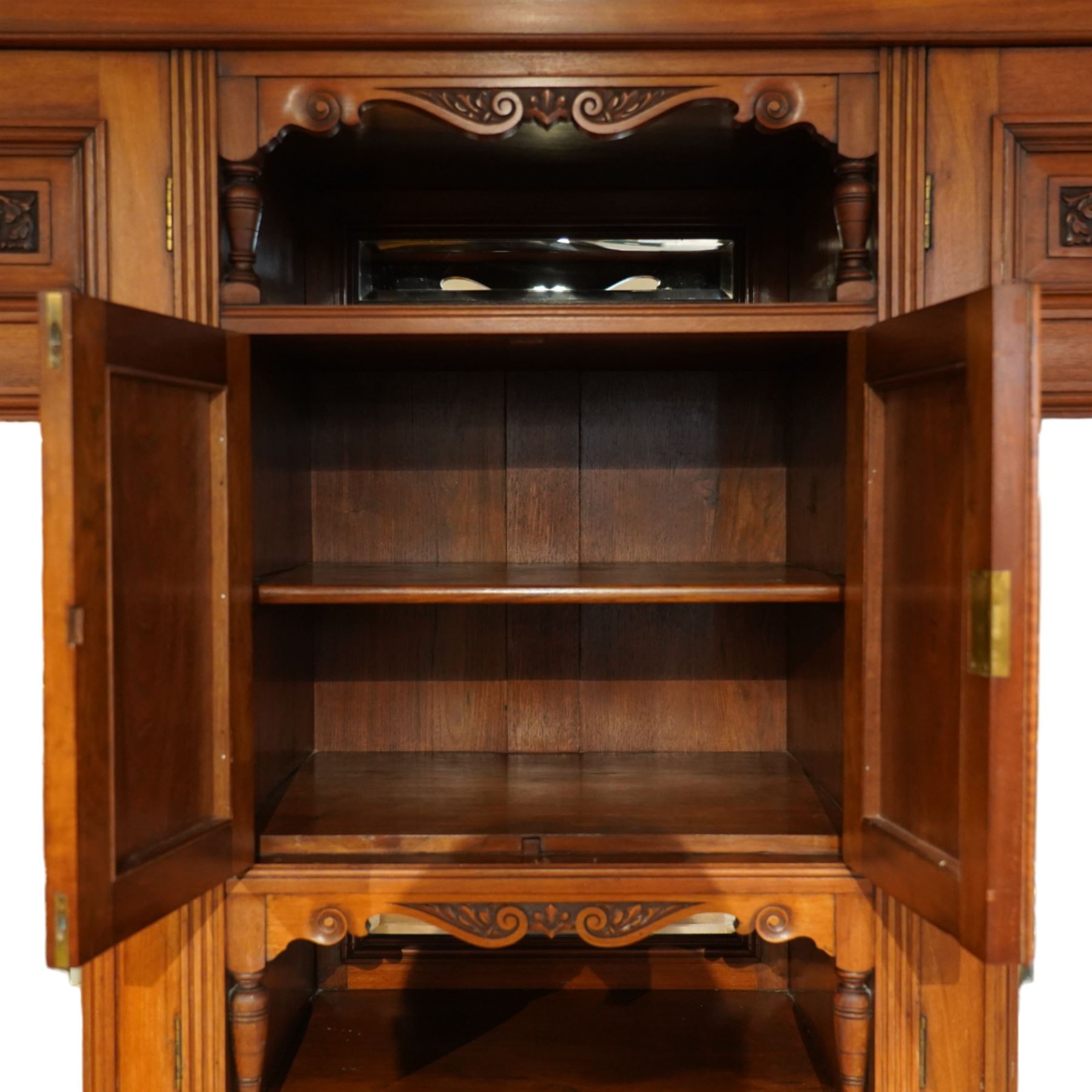 Edwardian walnut triple combination wardrobe, projecting pediment with pierced foliate scroll cresting above a central cupboard flanked by bevelled mirrored doors, the central section with twin panelled cupboard doors carved with foliate scrolls, over open recess with mirrored back and turned supports, above two short and three long drawers with brass handles, interior fitted with hanging rails and shelf, raised on plinth base
