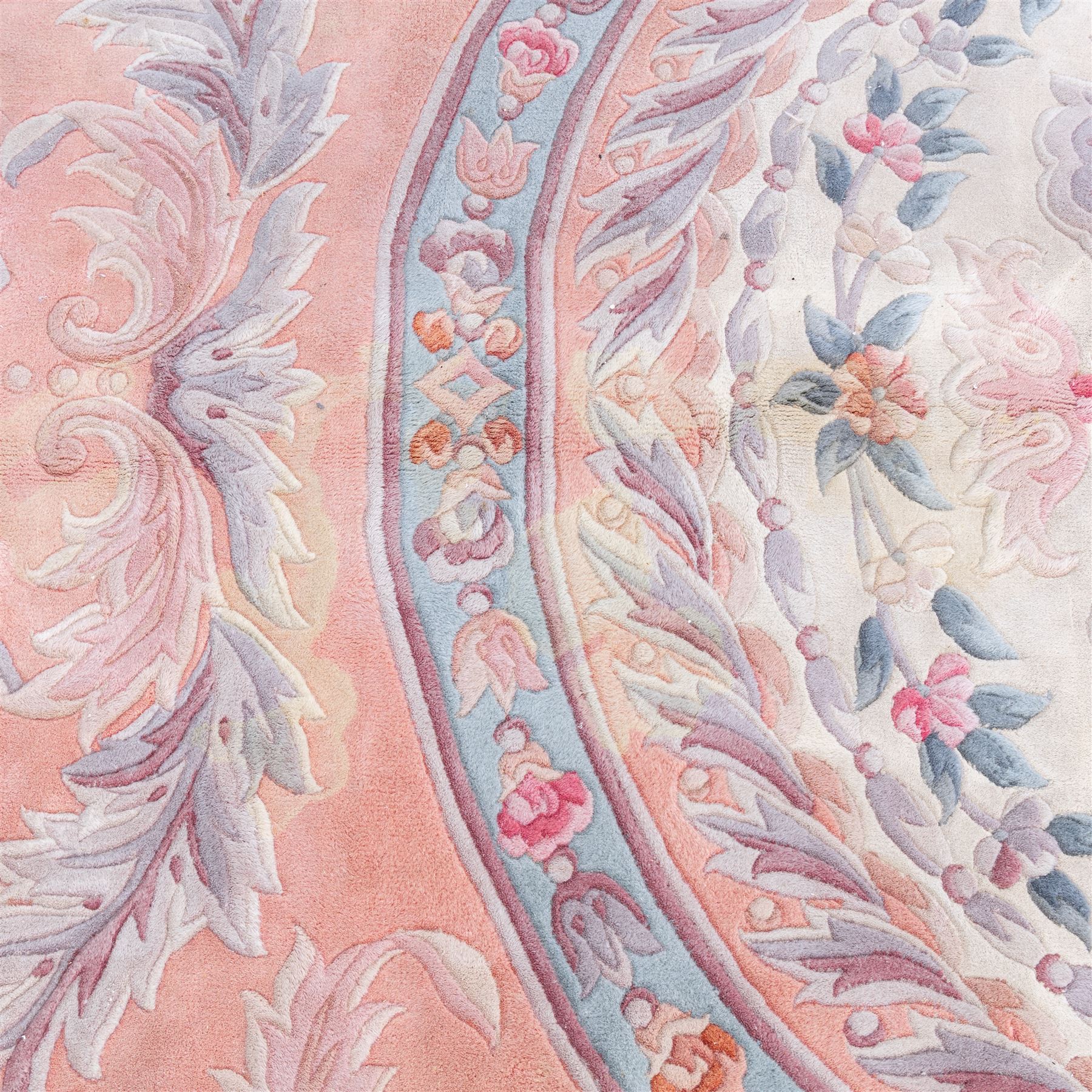 Large late 20th century Aubusson style wool carpet, peach and pastel toned field with central floral medallion enclosing scrolling acanthus and and foliate sprays, surrounding field decorated with further stylized foliage and and floral ornament, within shaped reserves and indigo corner spandrels, enclosed by narrow guard border, cotton fringe ends