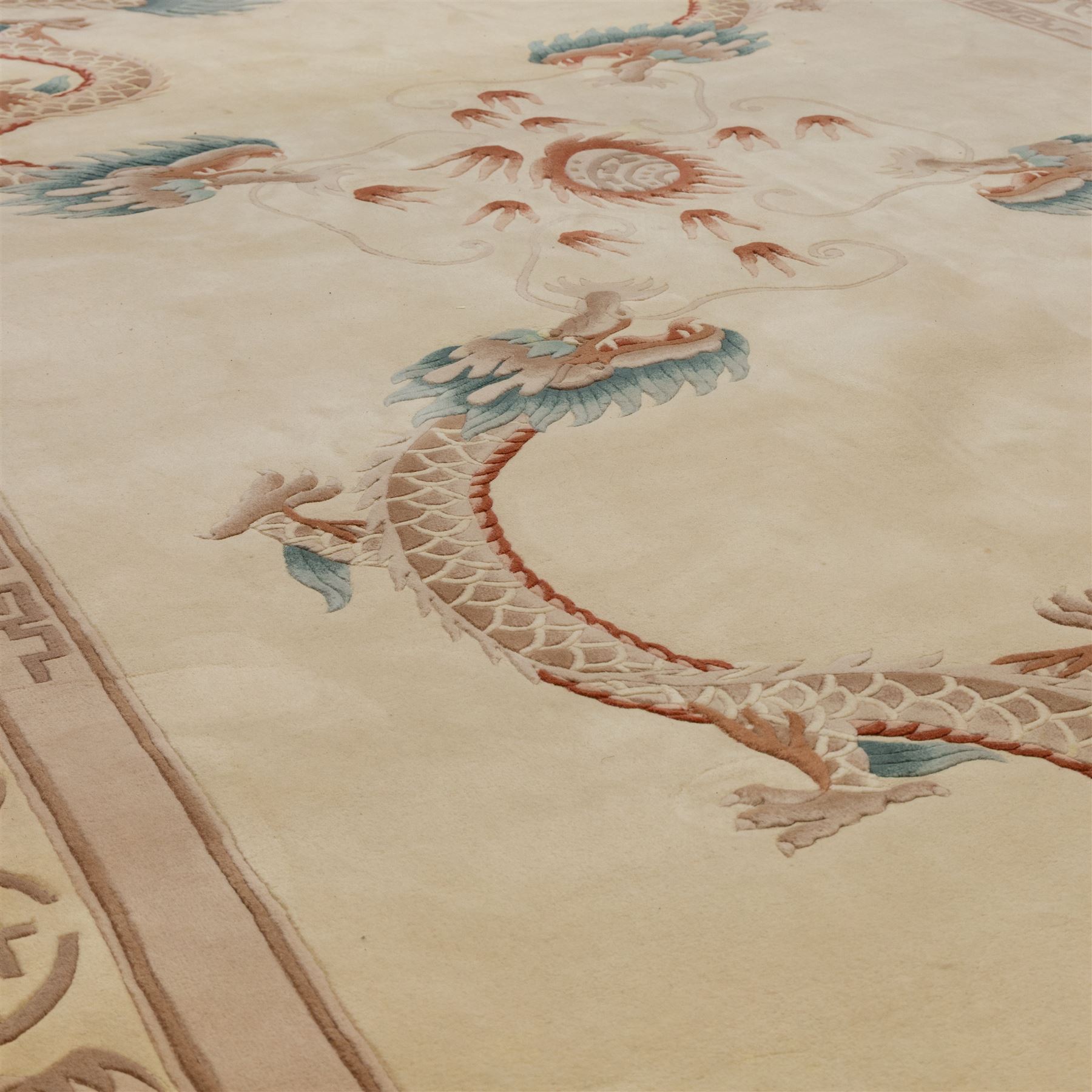 Late 20th century Chinese wool carpet, cream field with five stylized dragons arranged in a circular formation around a central flaming pearl motif, dragons depicted with elongated bodies and clawed feet amongst stylized cloud forms, enclosed within a narrow inner border and a wider outer border decorated with traditional Chinese motifs and symbols