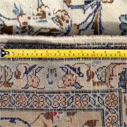 Large Central Persian Kashan hand-knotted carpet, ivory field with an all-over scrolling design of vines, palmettes, and floral sprays, enclosed by a broad camel-ground palmette and vine border, framed by multiple guard stripes in a palette of ivory, beige, blue and polychromed tones, with cotton fringe ends 