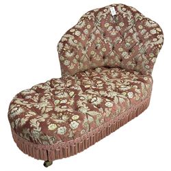 Early 20th century small chaise longue, scallop shaped back over sprung seat, upholstered in buttoned foliate patterned pink velour fabric with fringing, on turned supports with castors
