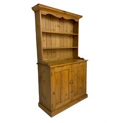 Pine dresser, raised rack fitted with two shelves, the base enclosed by two panelled doors and fitted with internal drawers, plinth base