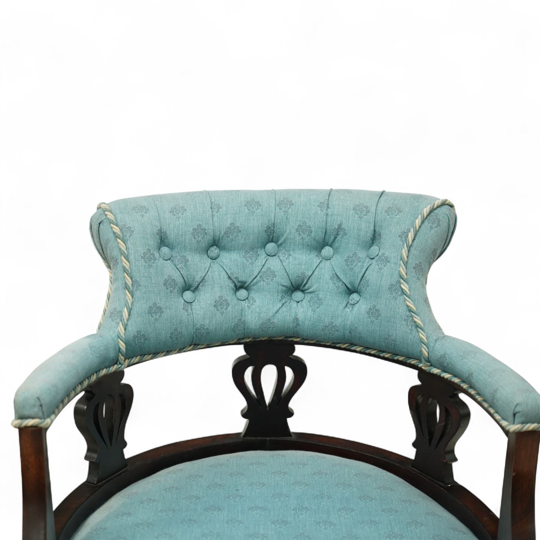Late Victorian mahogany upholstered tub chair, curved button-back with rope-edge trim over open shaped arms and pierced splat supports, rounded seat upholstered in patterned blue fabric, raised on cabriole front supports