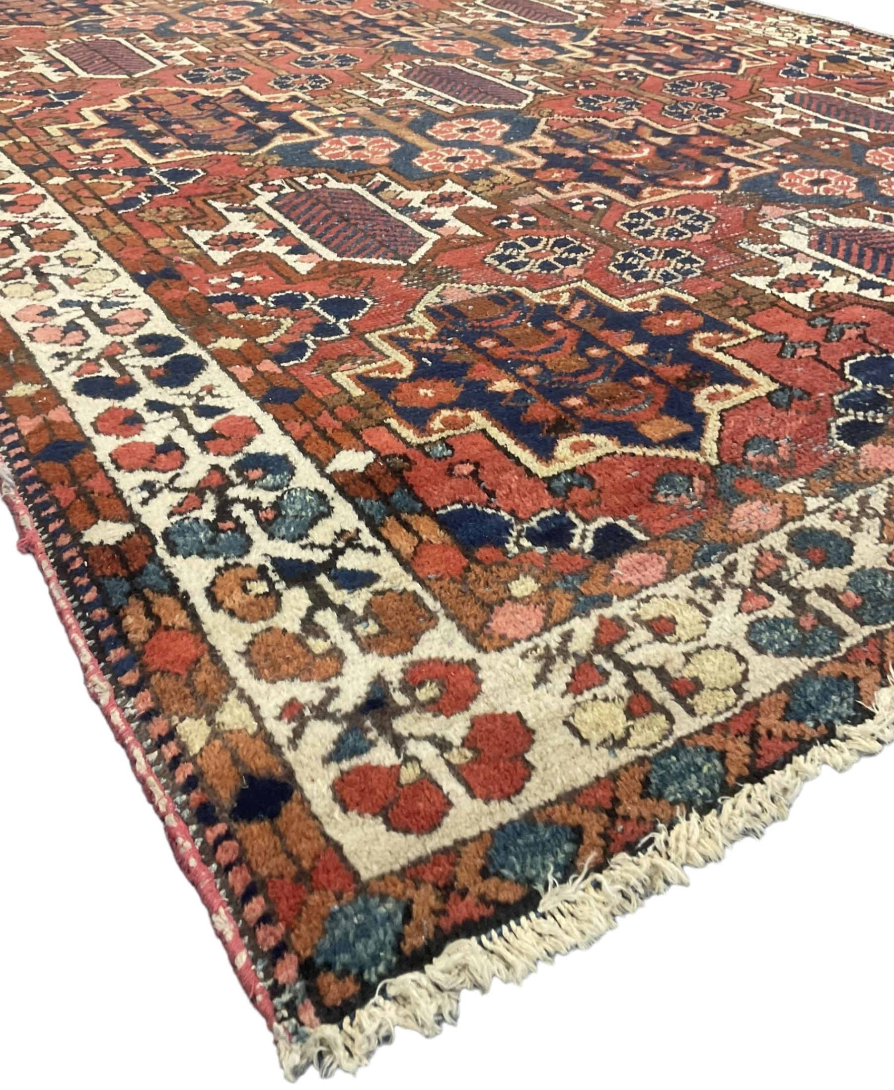 Persian crimson ground rug, the field decorated with three rows of stylised plant medallions and small flowerhead motifs, repeating floral design border with guards 