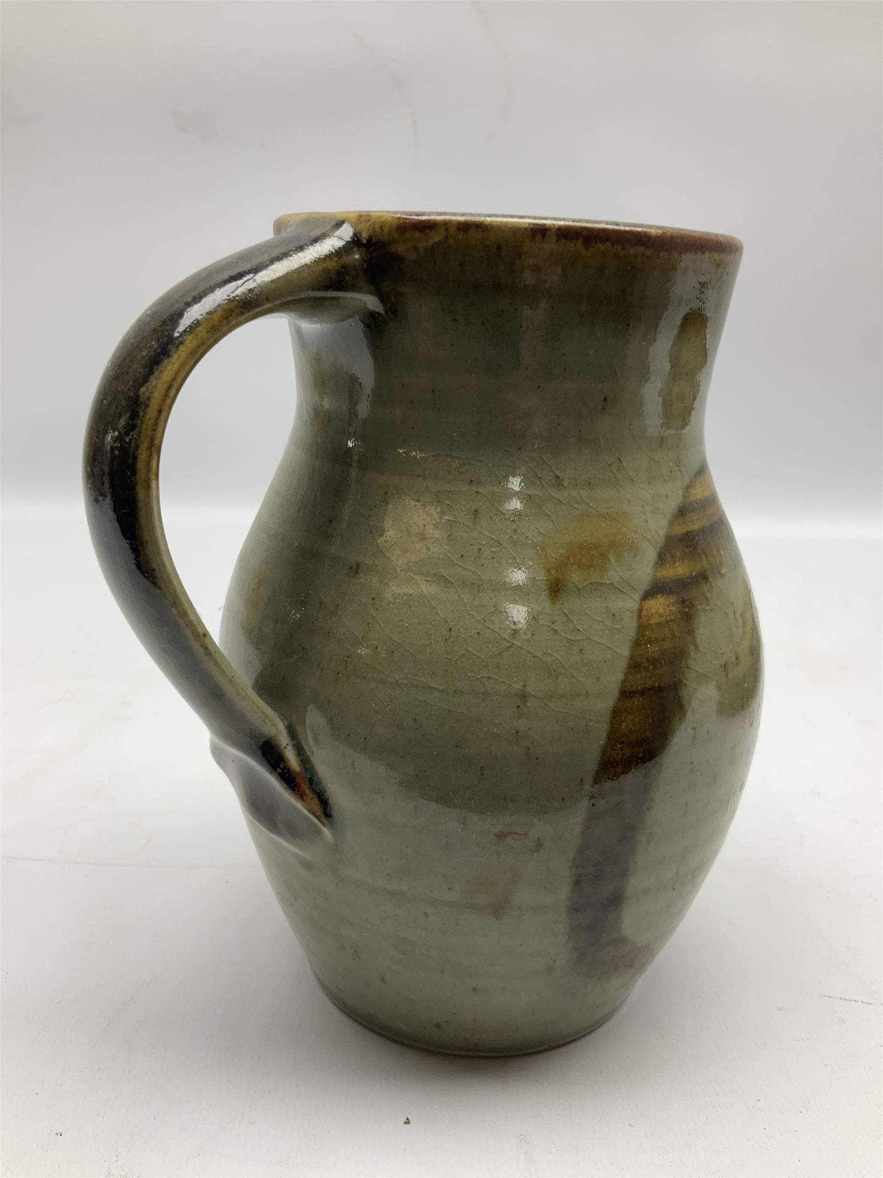 Michael Leach (British 1913-1985) for Yelland pottery; two large glazed stoneware plates with dark brown stylised decoration upon oatmeal ground, together with a jug in merging blue, green and brown, all with impressed marks beneath, largest plate D37cm