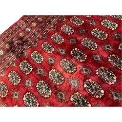 Pakistani Bokhara red ground rug, the field decorated with repeating Gul motifs and lozenges, the multi-band border with stylised plant motifs with dark indigo outlines