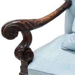 Carolean design walnut and oak wingback open armchair, the high wingback upholstered in light blue herringbone fabric, acanthus leaf carved arms with scrolled terminals and on scrolled supports, cane work seat with squab cushion and scatter cushion, the lower rail carved and pierced with putti holding crown surrounded by curled acanthus leaves, leaf carved S-scroll supports united by Scrolled X-framed stretchers 
