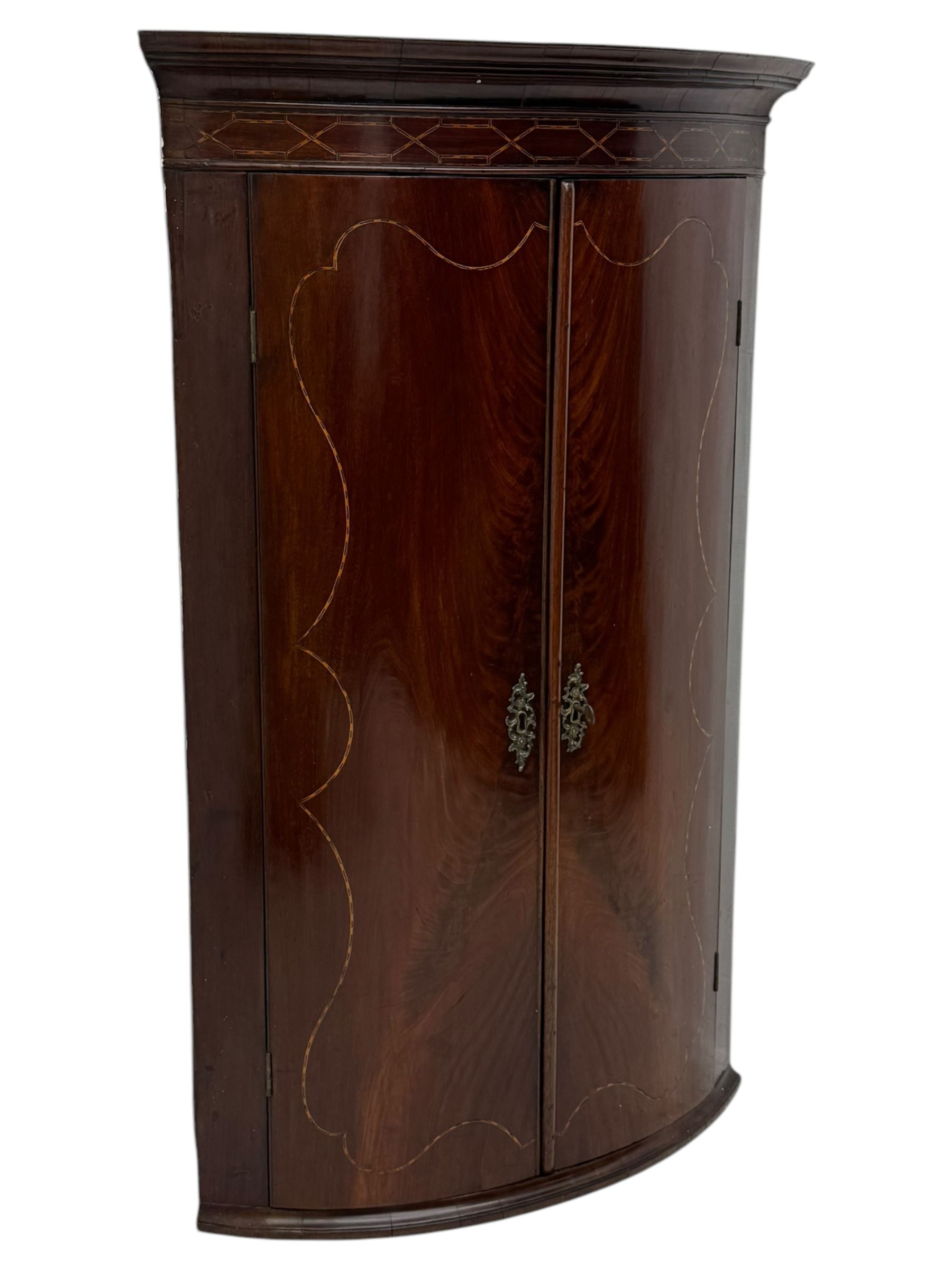 Late Georgian mahogany hanging corner cupboard, moulded cornice with interlaced boxwood stringing pattern above two cupboard doors inlaid with wave form boxwood stringing and four internal shelves 