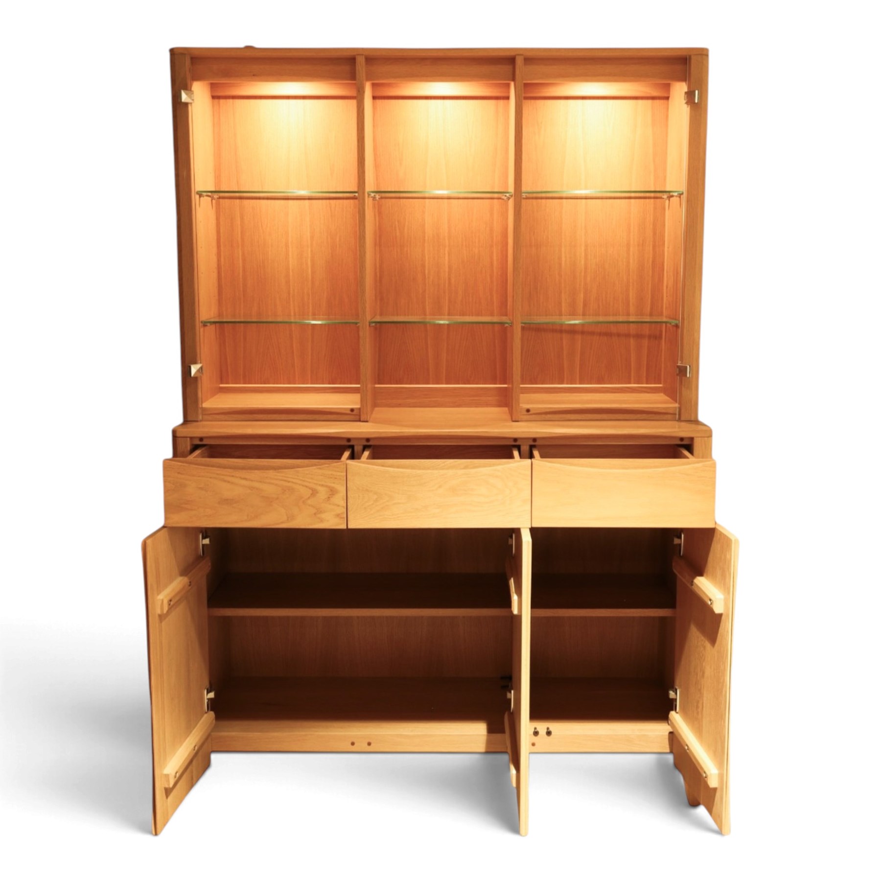 Ercol - 'Artisan' light oak dresser, upper section with cantered corners, with central open area fitted with adjustable glass shelves, flanked by twin glazed cabinets with further adjustable glass shelving, the lower section with three shorts drawers with recessed handles, above three cupboard doors with recessed handles enclosing adjustable wooden shelves, raised on short tapering supports 