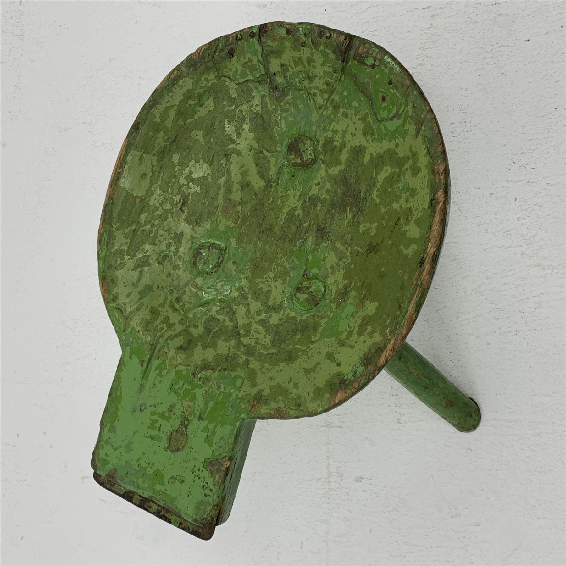 18th/19th century vernacular primitive green painted stool with dished seat fitted with metal scraper to one end, on three splayed legs, L46cm, H34cm