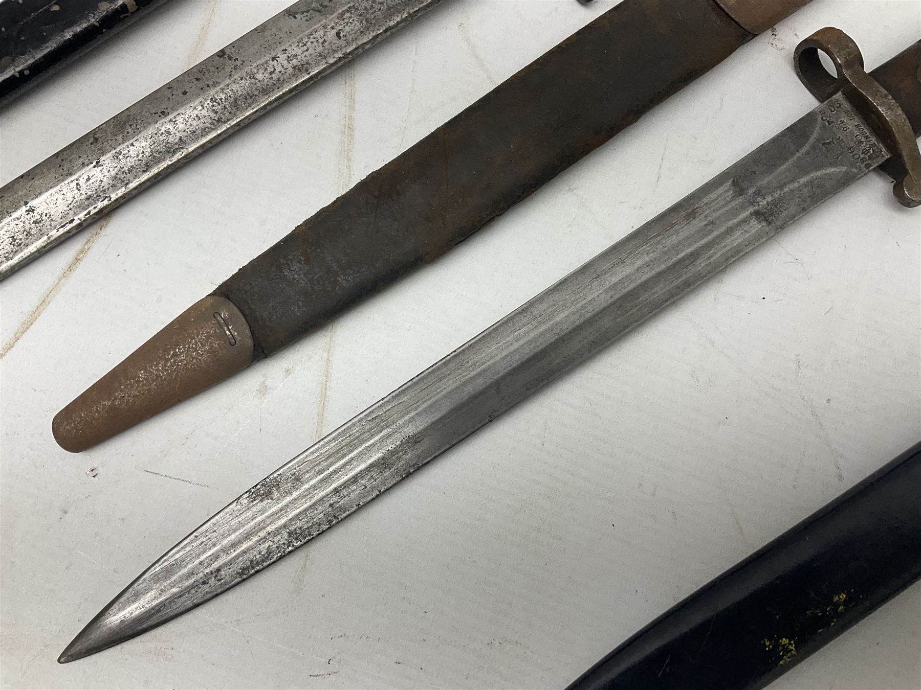 British No 7 MKI knife bayonet with 20cm single edged fullered clipped point blade;  blackened steel, large muzzle ring cross-guard; blackened swivelling pommel marked 'F5H'; red Tufnol composite grips; in blackened steel scabbard L33cm overall; British Pattern 1888 bayonet with scabbard; and German Ersatz bayonet with scabbard (3)