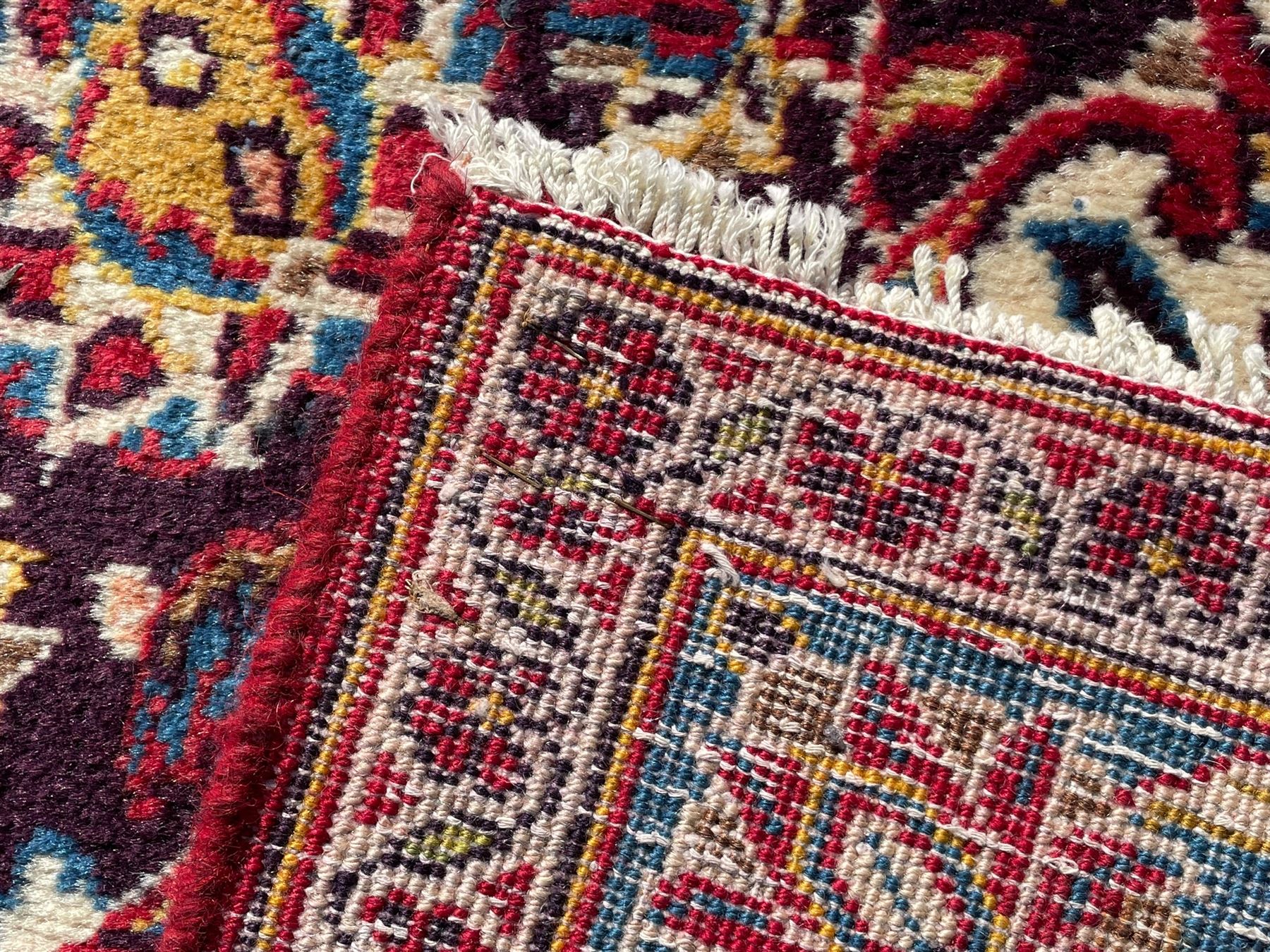 Large Persian Kashan crimson ground carpet, large floral central medallion surrounded by trailing branches decorated with leaves and stylised plant motifs, the main border with scrolling design interspersed with palmettes, within floral pattern guard stripes 